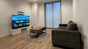 Ein modernes Wohnzimmer mit Flachbildfernseher, Couchtisch aus Holz und grauem Sofa.