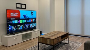 Ein modernes Wohnzimmer mit Flachbildfernseher, Holztisch und einem gemusterten Teppich.