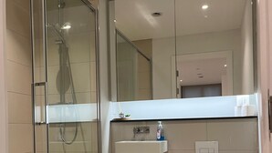 Ein modernes Badezimmer mit einer Duschkabine aus Glas, einem Waschbecken mit Spiegel darüber und einer Toilette.