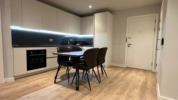 Eine moderne Küche mit integrierten Geräten, ein Essbereich mit Tisch und Stühlen und ein Holzboden.