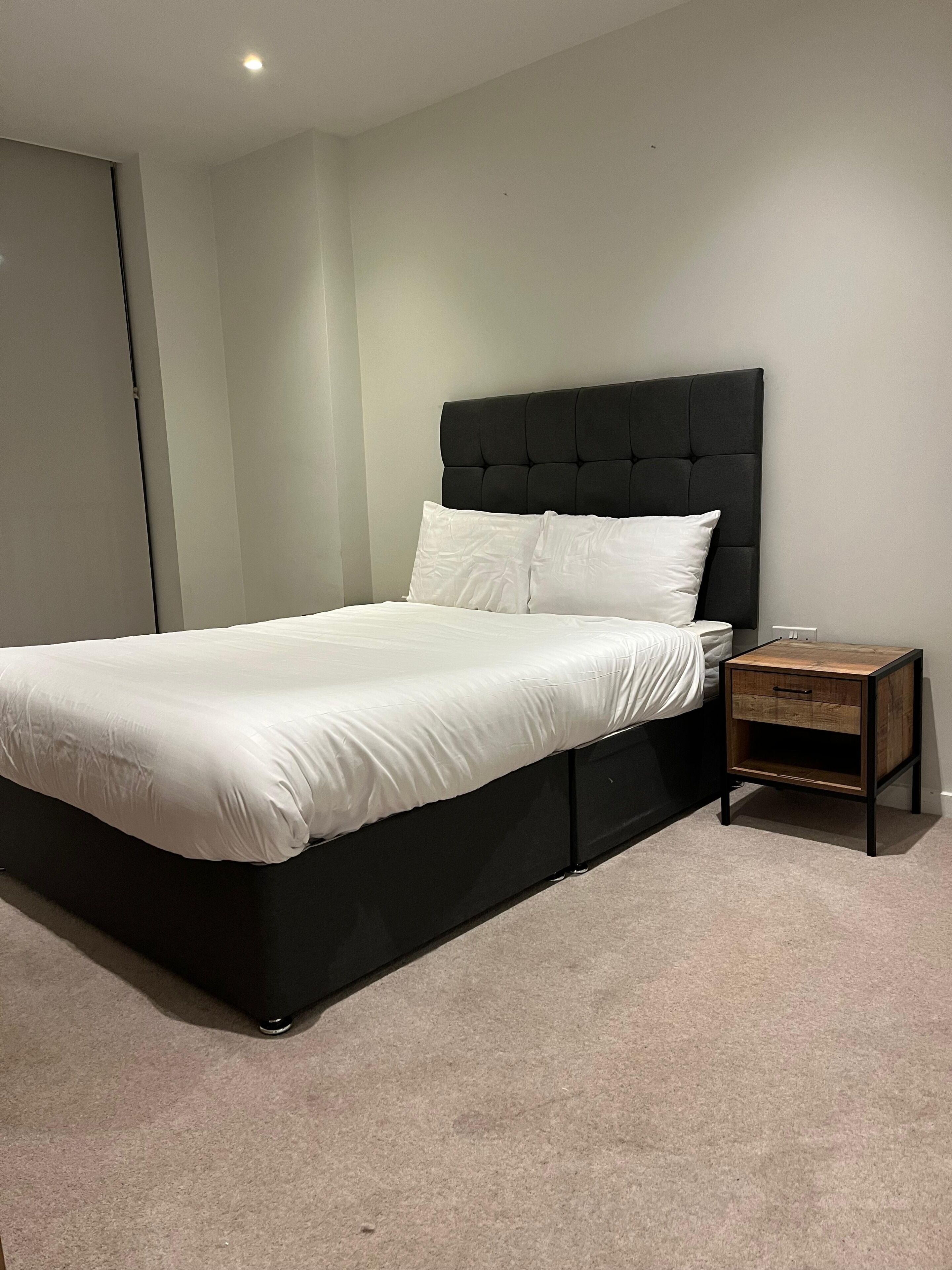Ein modernes Schlafzimmer mit einem großen Bett, einem Kopfteil, einem Nachttisch und einem Teppichboden.
