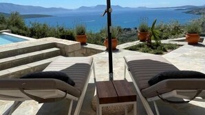 A poolside area with lounge chairs, a table, and an umbrella. - Grey Sea View Estate (Lefkada)