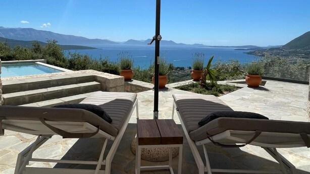 A terrace with lounge chairs and an umbrella overlooking a pool and scenic mountains. - Grey Sea View Estate (Lefkada)