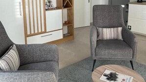 A modern office space with two grey upholstered chairs, a wooden shelving unit, and a small round table with a magazine. - Grey Sea View Estate (Lefkada)