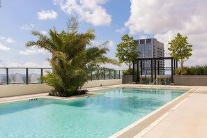 A rooftop swimming pool with a clear view of the city skyline, surrounded by palm trees and a modern building. - Miami 1BR Getaway for 4 Guests at The Crosby (Miami)