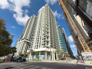 A high-rise building with multiple floors, a construction crane, and a street with cars and palm trees. - Miami 1BR Getaway for 4 Guests at The Crosby (Miami)