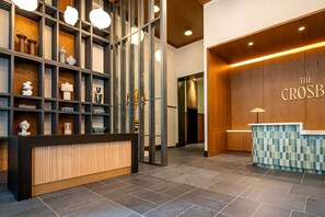 A reception area with a wooden reception desk, a tiled wall with a mosaic pattern, and a shelving unit with various decorative items. - Miami 1BR Getaway for 4 Guests at The Crosby (Miami)