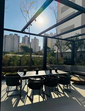 Um pátio externo com mesas e cadeiras, vista para edifícios altos e céu claro.
