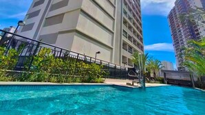 Un hotel alt amb un distintiu dibuix en forma de V a la façana, una piscina al primer pla i altres edificis al fons.