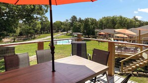A wooden deck with a table and chairs, an orange umbrella, and a view of a pool and trees. - Skyline Cabin - Lakefront Table Rock Lake (Galena)