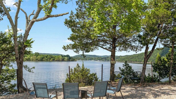 Un espace aménagé au bord du lac, avec des chaises et une table, entouré d’arbres et offrant une vue sur le lac.