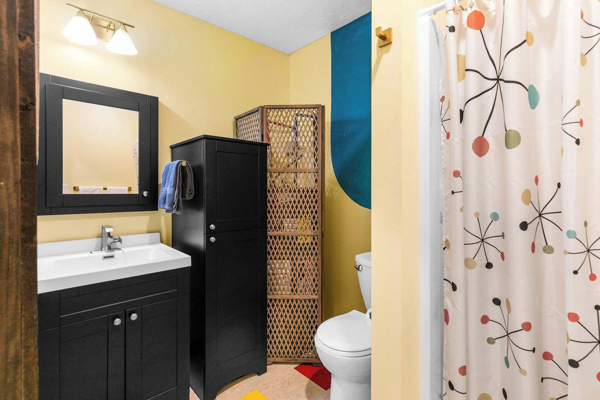Une salle de bain équipée d’un lavabo, d’un miroir, de toilettes, d’un rideau de douche et d’une cloison décorative.