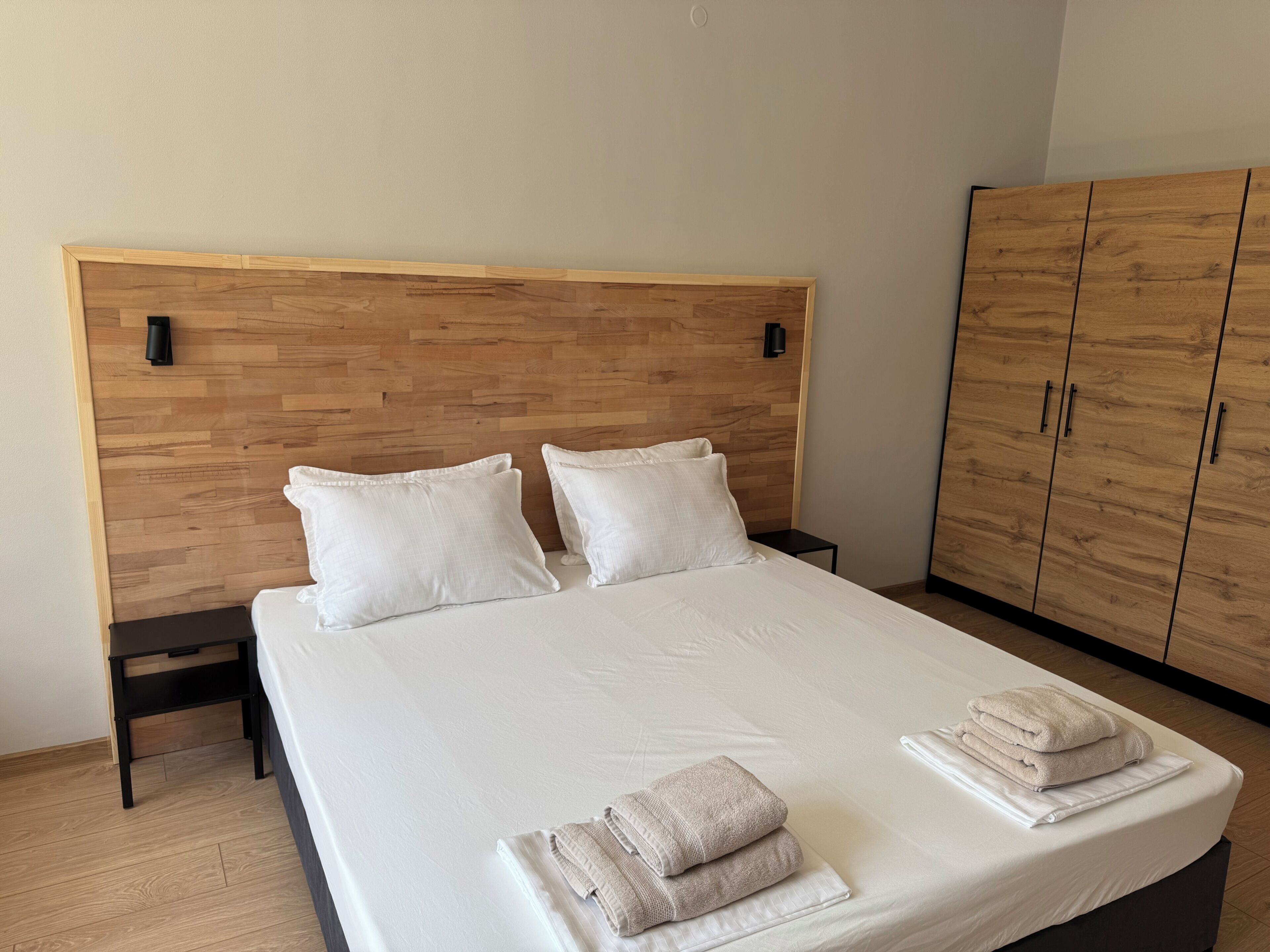 Cama bem arrumada com almofadas, mesa de cabeceira e guarda-roupa num quarto de hotel.