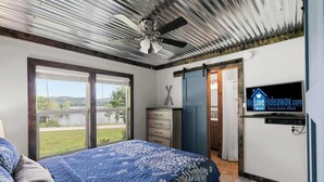 Una camera da letto con un letto, un ventilatore a soffitto, una TV, una finestra e una porta che dà su un'altra stanza.