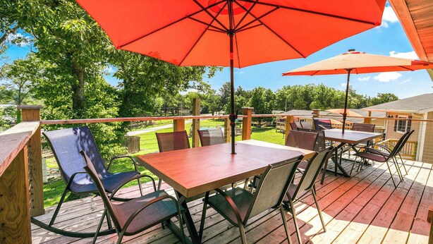 Eine Holzdielen-Terrasse mit Tisch, Stühlen und Sonnenschirm, mit Blick auf einen Garten.