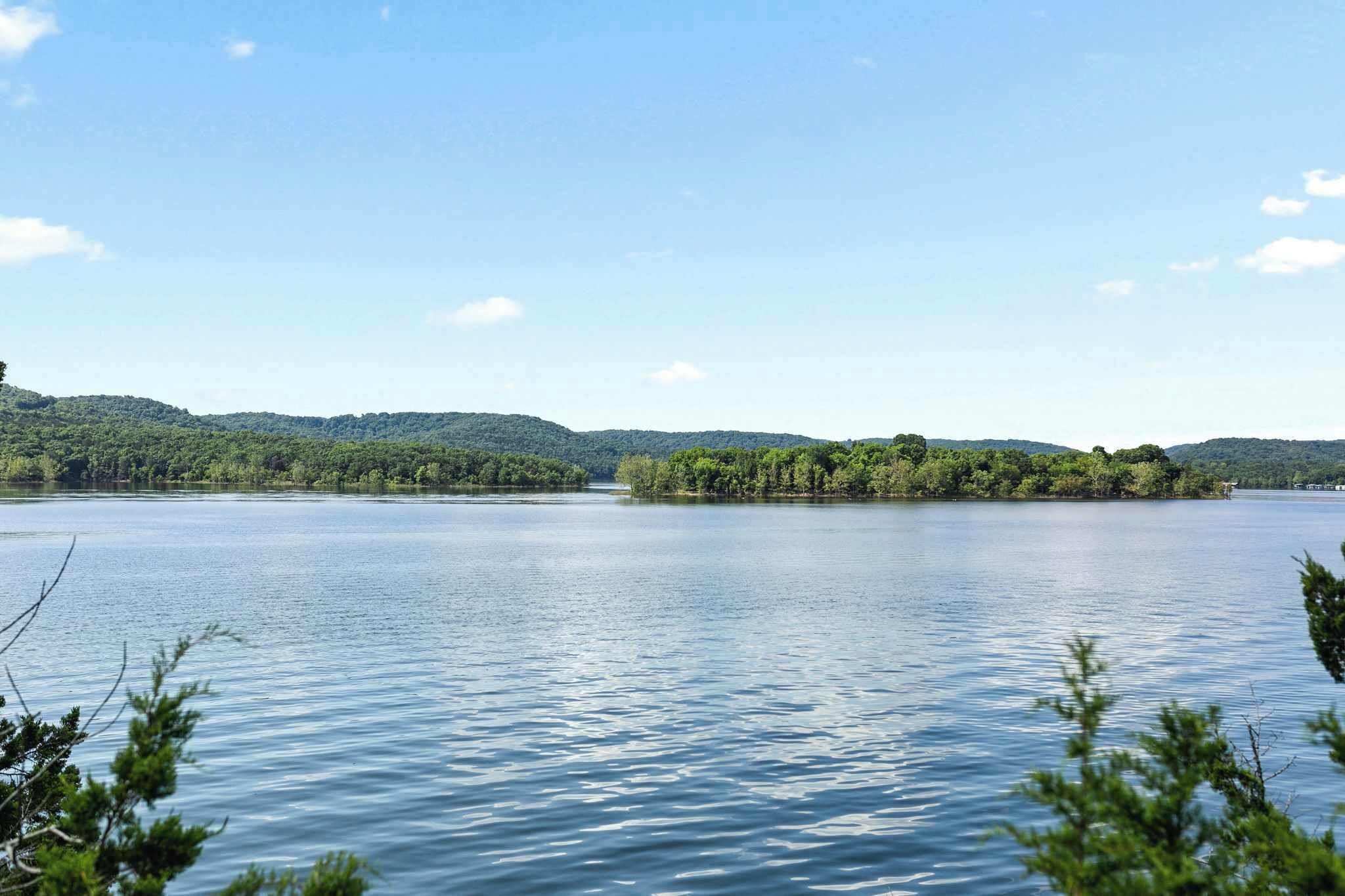 A calm lake with a small island in the center, surrounded by forested hills.