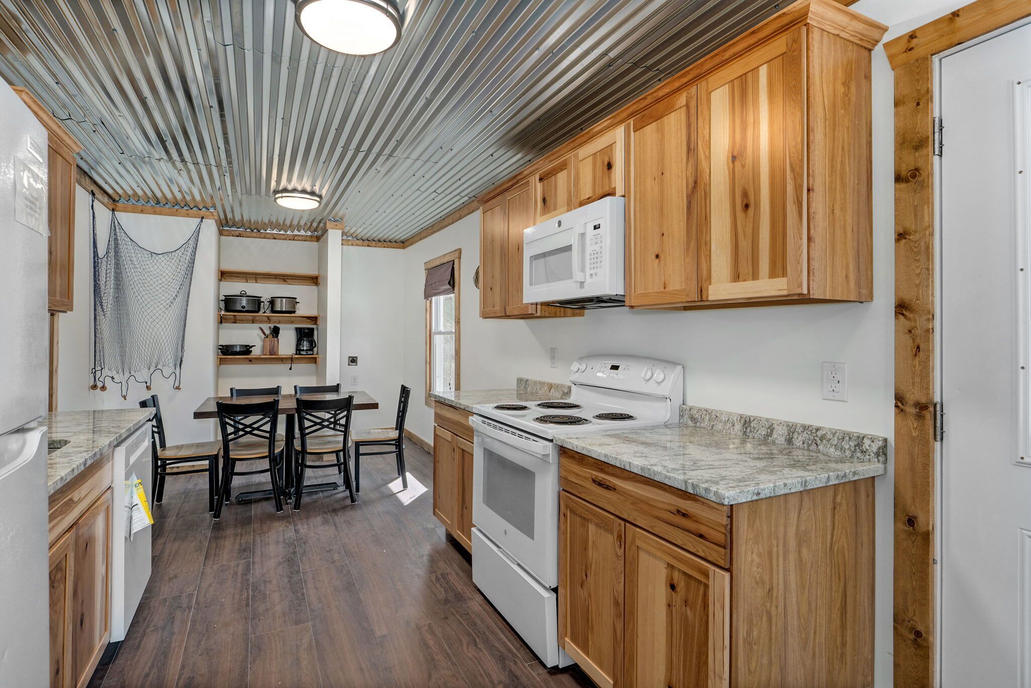A compact kitchen with wooden cabinets, a white stove, a microwave, and a dining area with a table and chairs.