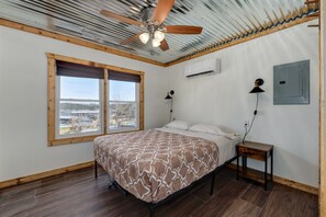 A bedroom with a bed, a window, a ceiling fan, and an air conditioning unit. - Blue Heron · Lakefront Cabin · Pool & Dock (Galena)
