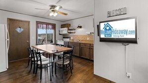 A kitchen with a dining table, chairs, a ceiling fan, a microwave, and a TV displaying a website. - Crest View Cabin - Lakefront Table Rock Lake (Galena)
