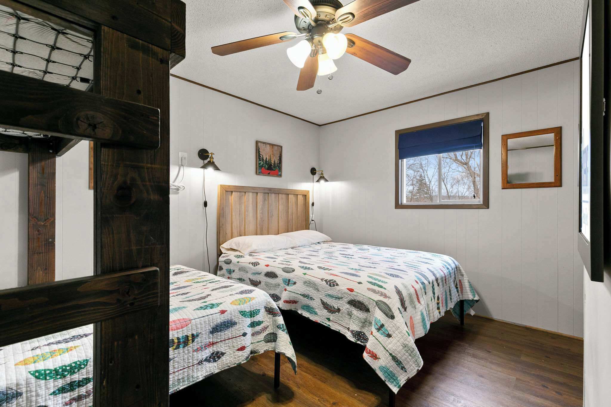 Un dormitorio con dos camas, un ventilador de techo, una ventana con vistas y un cabecero de madera.