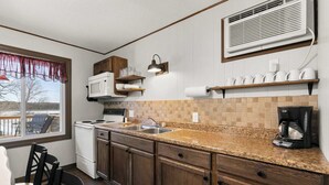 A compact kitchen with a microwave, stove, sink, and a coffee maker. There are wooden cabinets, a window with a view, and a ceiling vent. - Crest View Cabin - Lakefront Table Rock Lake (Galena)