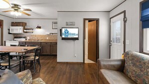 A kitchen with a microwave, stove, and wooden cabinets, a dining area with a table and chairs, a sofa, and a ceiling fan. - Crest View Cabin - Lakefront Table Rock Lake (Galena)