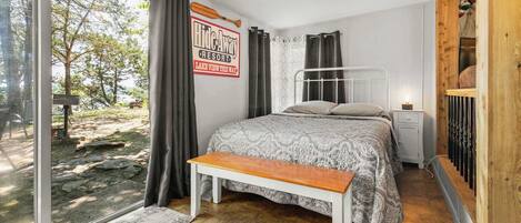 A bedroom with a bed, a bench, a nightstand, a ceiling fan, and a view of the outdoors.