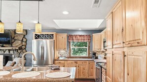 Une cuisine dotée de meubles en bois, d’un réfrigérateur en acier inoxydable, de plans de travail en granit et de luminaires suspendus.