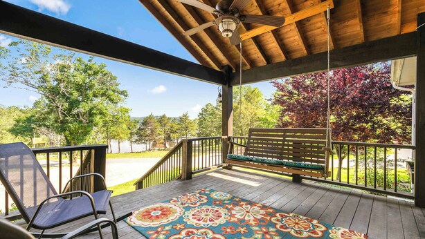 Une véranda couverte avec un plafond en bois, un ventilateur de plafond, un banc et un tapis coloré.