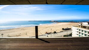 Vista sulla spiaggia da un edificio con terrazza in legno, spiaggia sabbiosa, oceano e una nave in lontananza.