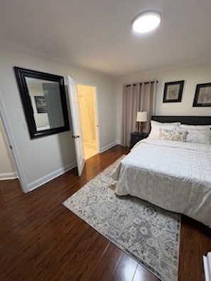 Un dormitorio con cama, mesita de noche, lámpara, espejo y puerta.