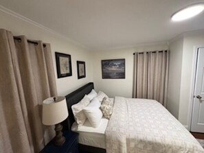 Une chambre à coucher avec un lit, des rideaux, une table de chevet, une lampe et des tableaux encadrés accrochés au mur.