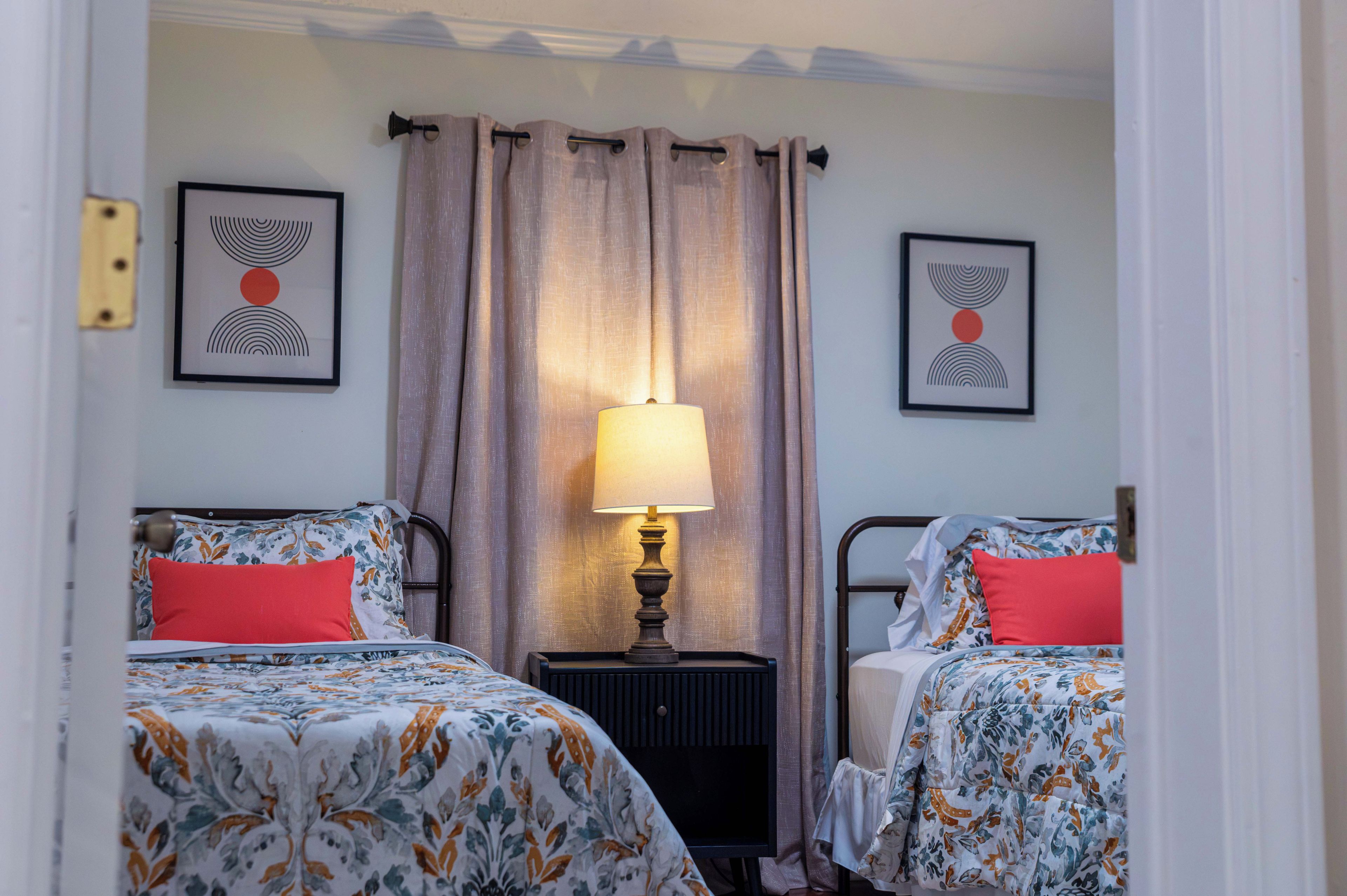 Une chambre d’hôtel avec deux lits, une table de chevet avec une lampe et deux œuvres d’art abstraites encadrées accrochées aux murs.