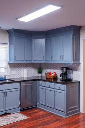 A kitchen with grey cabinets, a herringbone tile backsplash, a coffee maker, and a basket of items on the countertop. - Mint Hill Luxury Retreat / Near Charlotte/4BR/3BA (Mint Hill)