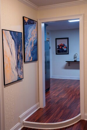 A hallway with a wooden floor, a refrigerator, and two abstract paintings on the wall. - Mint Hill Luxury Retreat / Near Charlotte/4BR/3BA (Mint Hill)