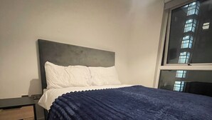 Et soveværelse med en seng, et natbord, et vindue og en vægmonteret lampe.