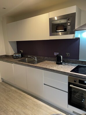 A modern kitchen with a built-in microwave, toaster, sink, and stove. - City Centre access - Stunning 2 Bed Retreat (Salford)