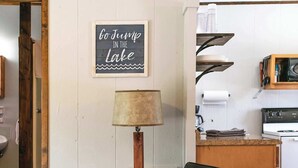 Una sedia di legno con un cuscino, una lampada e un cartello appeso al muro.