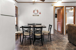 Un comedor con mesa y sillas, un refrigerador y un letrero en la pared que indica senderos de senderismo.