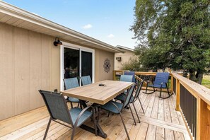 A deck with a wooden table and chairs, a sliding glass door, and a view of a tree.