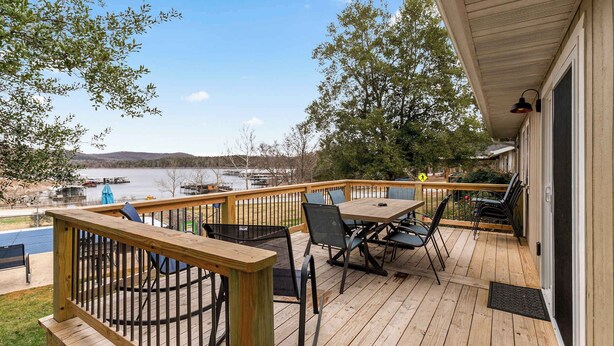 Une terrasse en bois avec des meubles d’extérieur, une vue sur un lac et des bateaux amarrés.