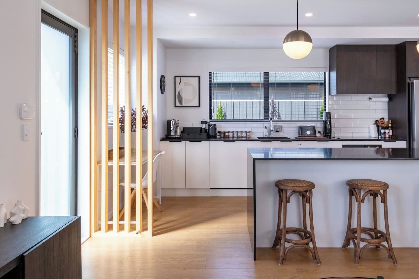 A modern kitchen with a central island, wooden stools, and a large window.