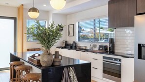 Cozinha moderna com ilha central, banquetas, máquina de café e vista para o exterior.