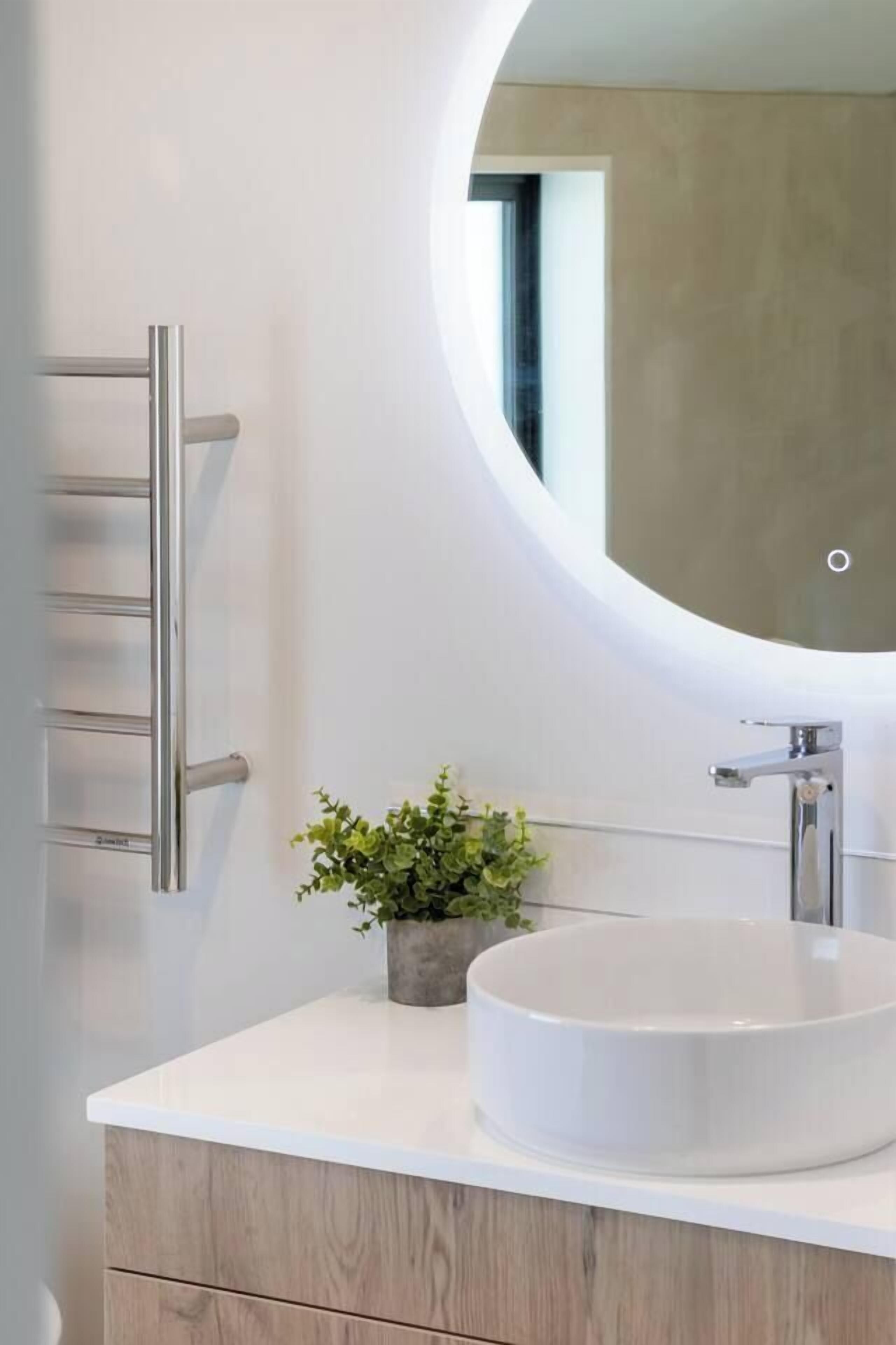 A modern bathroom with a round mirror, a white sink, a towel rack, and a small potted plant.