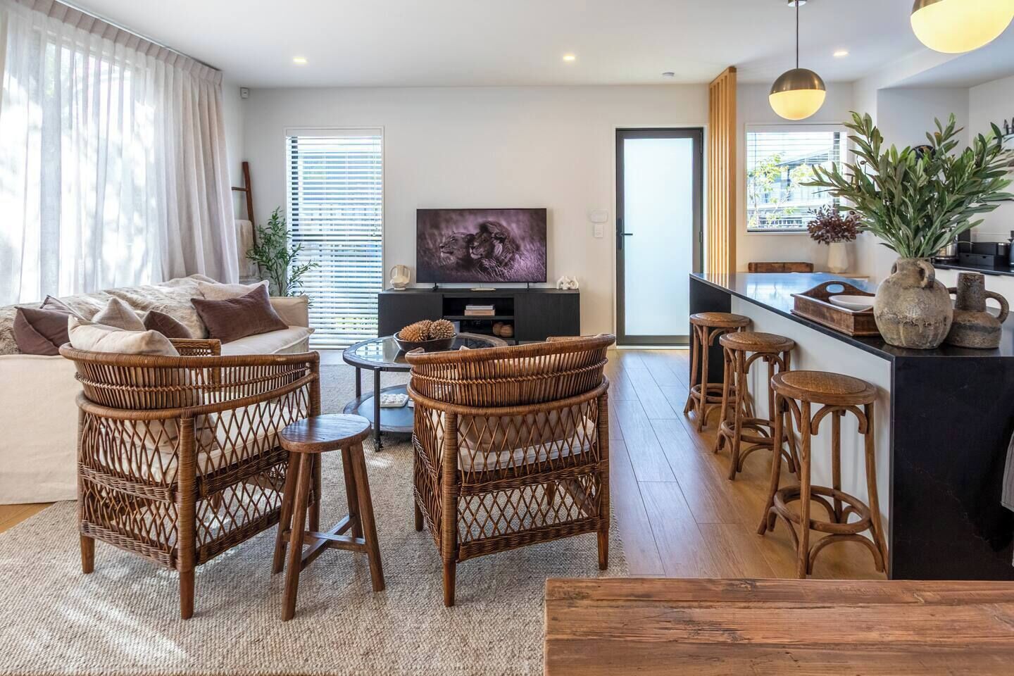Ein modernes Wohnzimmer mit Rattanmöbeln, einem Flachbildfernseher und einer Küchenzeile mit Barhocker.