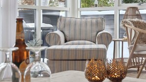 Ein Zimmer mit einem gestreiften Sofa, einem Korbstuhl und dekorativen Vasen auf einem Tisch.