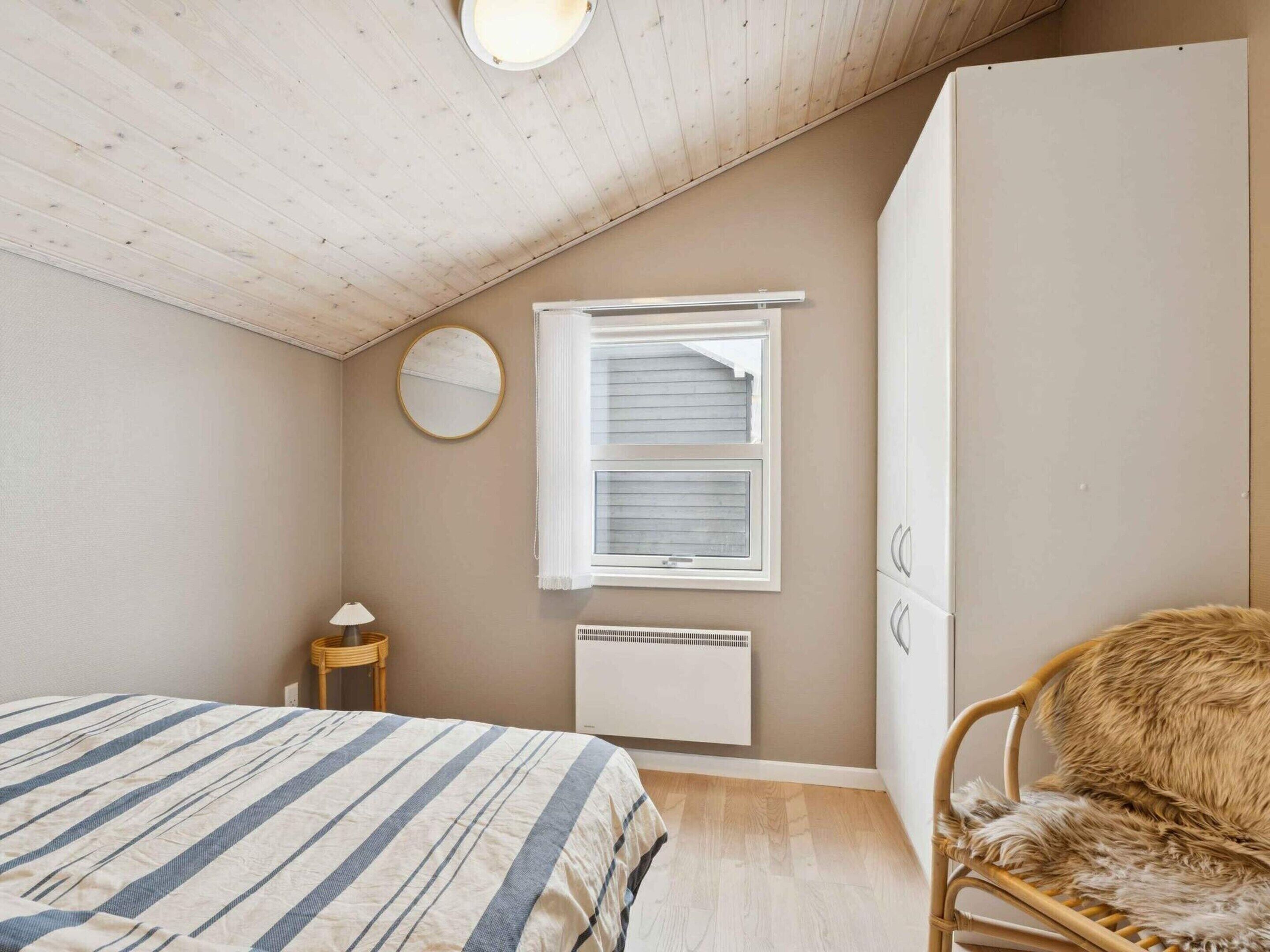 Ein Schlafzimmer mit einem Bett, einem runden Spiegel, einem Fenster mit Jalousien, einem Heizkörper und einem Kleiderschrank.