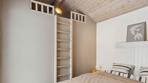 A bedroom with a bed, a wooden ladder, a white wall, and a framed picture. - 4 Star Holiday Home in Albaek (Aalbaek)