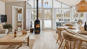A spacious living area with a large fireplace, a dining table set for four, and a cozy seating arrangement. - 4 Star Holiday Home in Albaek (Aalbaek)