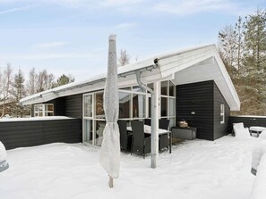 Ein modernes Haus mit überdachter Terrasse, großen Fenstern und einem mit Schnee bedeckten Dach.